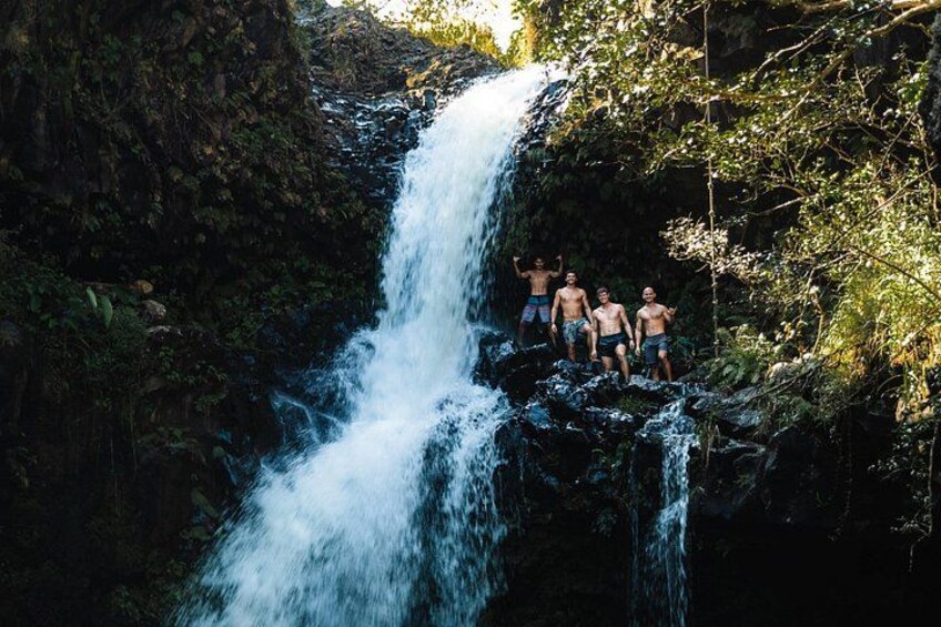 A waterfall with people standing on a rock ledge. 4