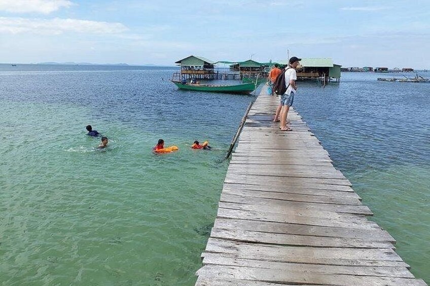 A wooden pier extending into calm waters with people swimming and standing on it. 2