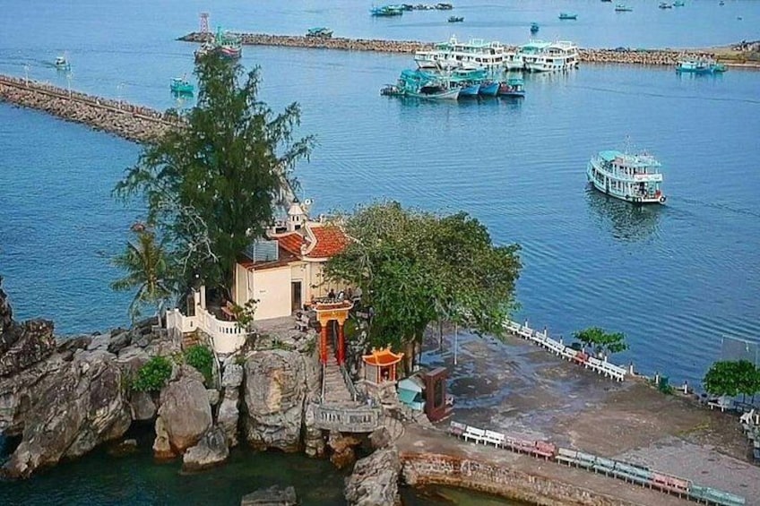 Zona costera con un pequeño templo, terreno rocoso y un puerto con barcos. 5