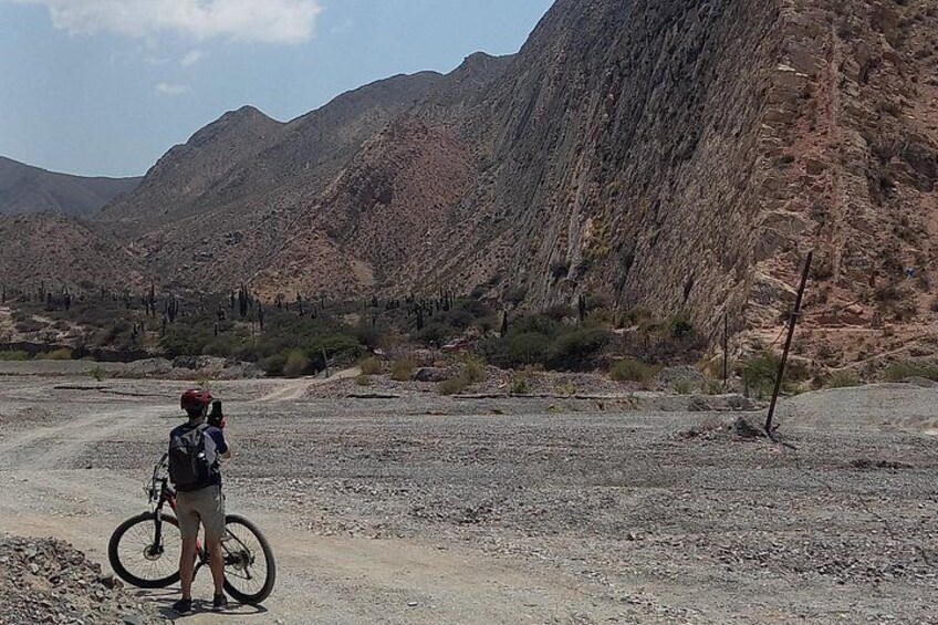 Une personne se tient sur un chemin de terre, à côté d’un vélo, et est entourée d’un paysage montagneux. 4