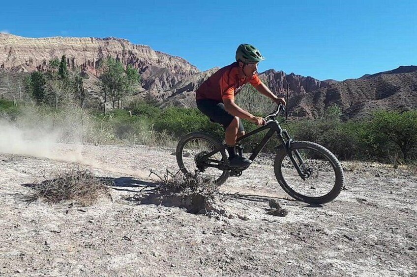 Une personne fait du vélo tout terrain sur un sentier accidenté, avec un paysage désertique en arrière-plan. 1