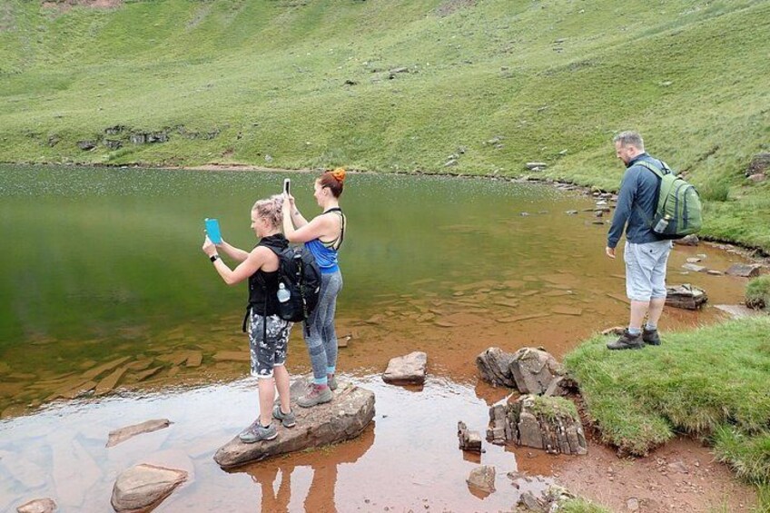 Tres personas en rocas a la orilla de un lago tranquilo, una tomando una fotografía. 4