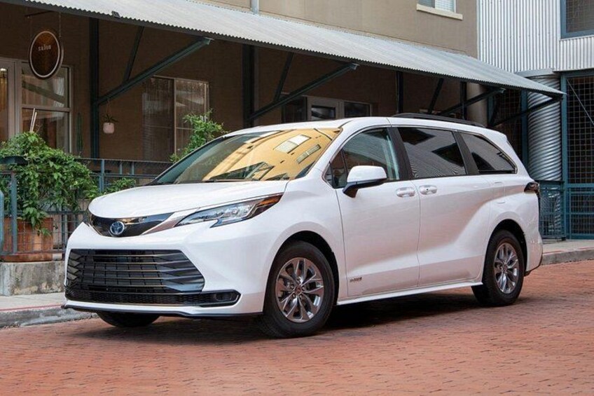 A white minivan parked on a brick pavement in front of a building with a metal awning. 4