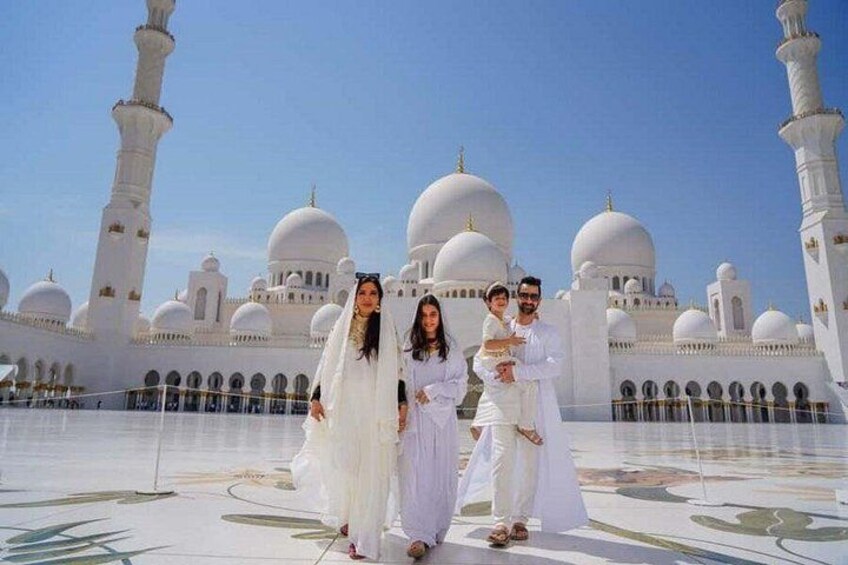 A group of people in traditional attire standing in front of a large white building with domes and minarets. 4