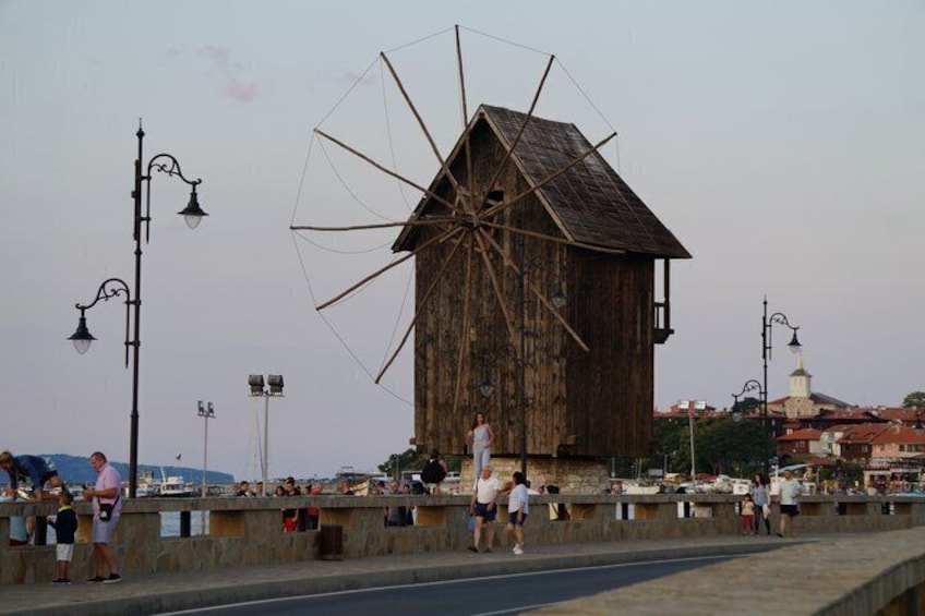 Un grand moulin à vent en bois, un mur de pierre et une étendue d’eau où se trouvent des bateaux. 5