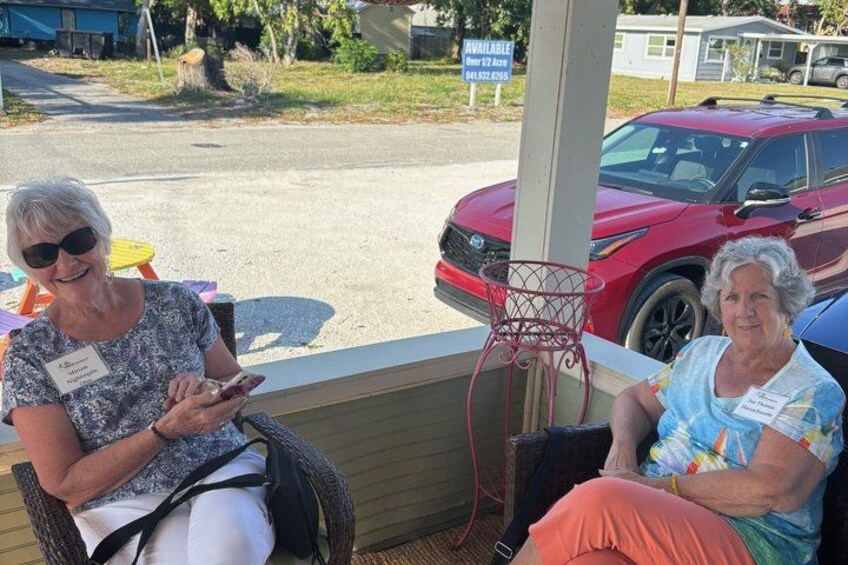 Dos personas sentadas en sillas, un coche rojo y un coche azul estacionados al fondo. 3