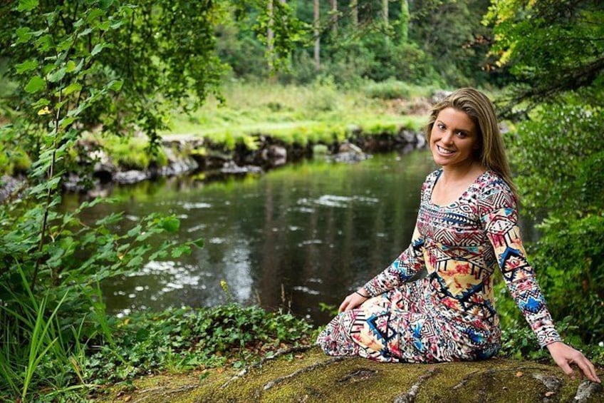 A person sitting on a moss-covered rock by a calm river surrounded by lush greenery. 2