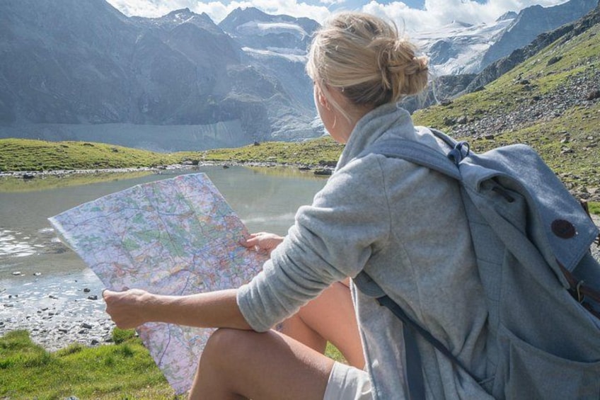 A person sitting by a lake with mountains in the background, holding a map. 3