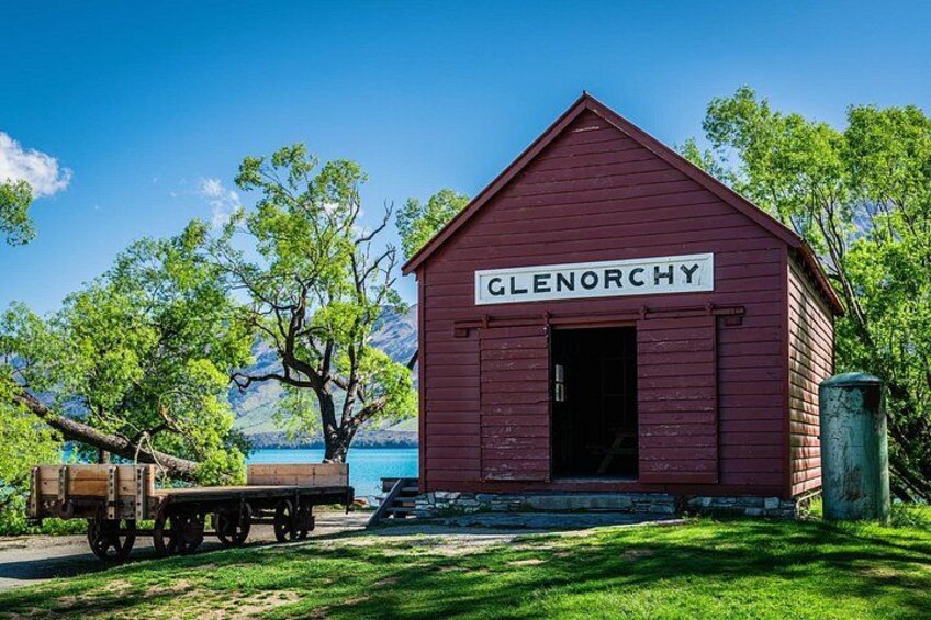 En röd byggnad som heter ”Glenorchy”, med en vagn av trä i närheten, och i bakgrunden syns träd och en klarblå himmel. 1