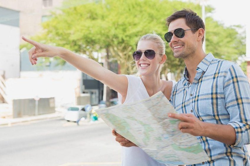 A couple holding a map, pointing at something off-camera, with a street and buildings in the background. 5