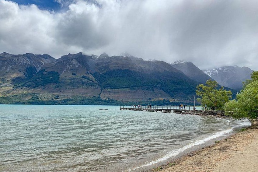 A lake with a wooden pier extending into the water, surrounded by mountains and a cloudy sky. 2