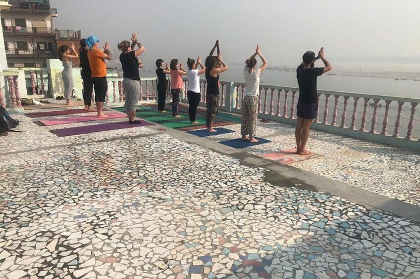 A group of people practicing yoga on a tiled outdoor platform with a railing and a view of the water. 4
