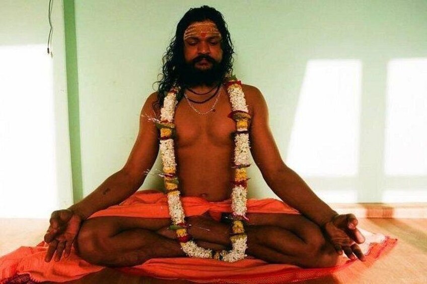 A person sitting cross-legged on a red mat, wearing a white garment and a garland of flowers. 1