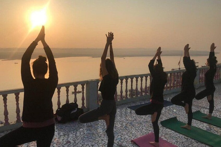 People practicing yoga on mats by a waterfront during sunrise. 3