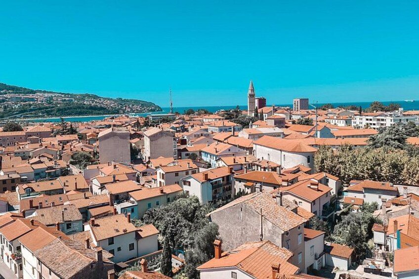 A coastal town with red-roofed buildings, a prominent tower, and a clear blue sky. 2