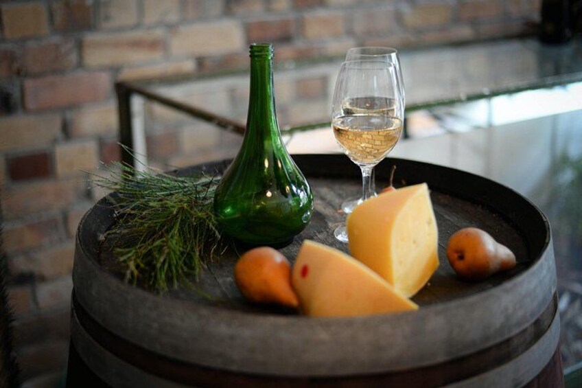A rustic setting with a green bottle, a glass of white wine, cheese, and a pear on a barrel. 1