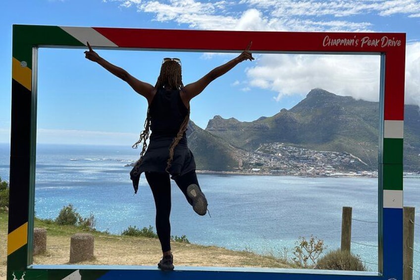 A person standing with arms raised, a scenic coastal landscape with mountains in the background, and a clear sky. 5