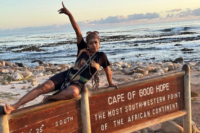 Una persona sentada en un banco con un cartel que dice 'Cape of Good Hope'. 5