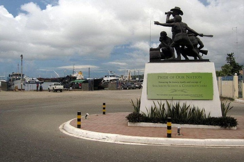 A statue of a soldier with a rifle, a plaque reading 'Pride of Our Nation,' and a marina with boats in the background. 3