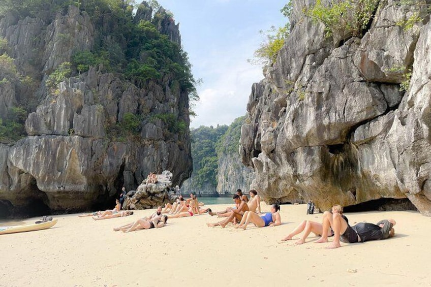 A beach with people sunbathing, large rock formations, and a clear sky. 2
