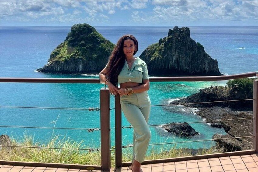 A person standing on a balcony overlooking turquoise waters with rocky islands in the distance. 4