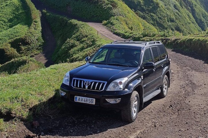 Un SUV nero parcheggiato su una strada sterrata, circondato da colline verdi e rigogliose. 2