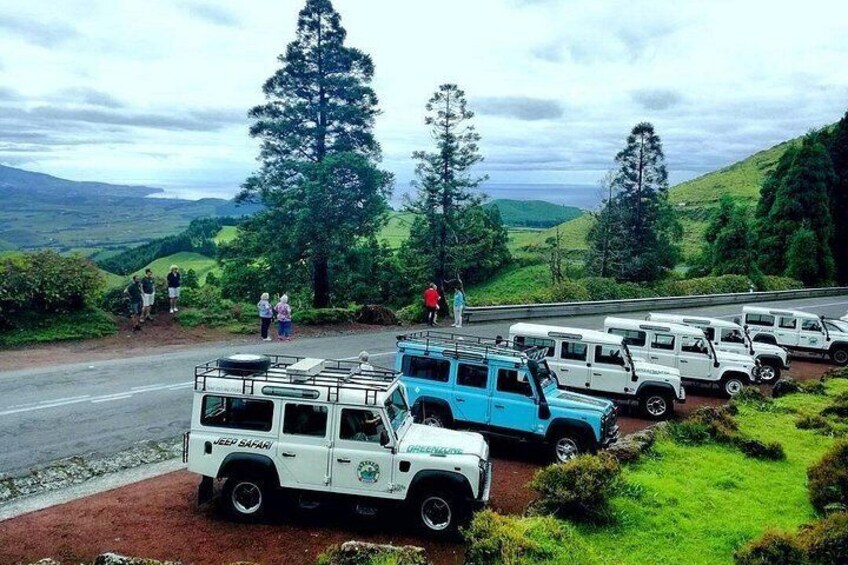 A line of safari vehicles parked on a road with a scenic landscape in the background. 2