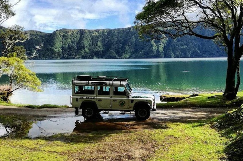 Un veicolo fuoristrada bianco parcheggiato vicino a un lago, con un albero e montagne sullo sfondo. 5