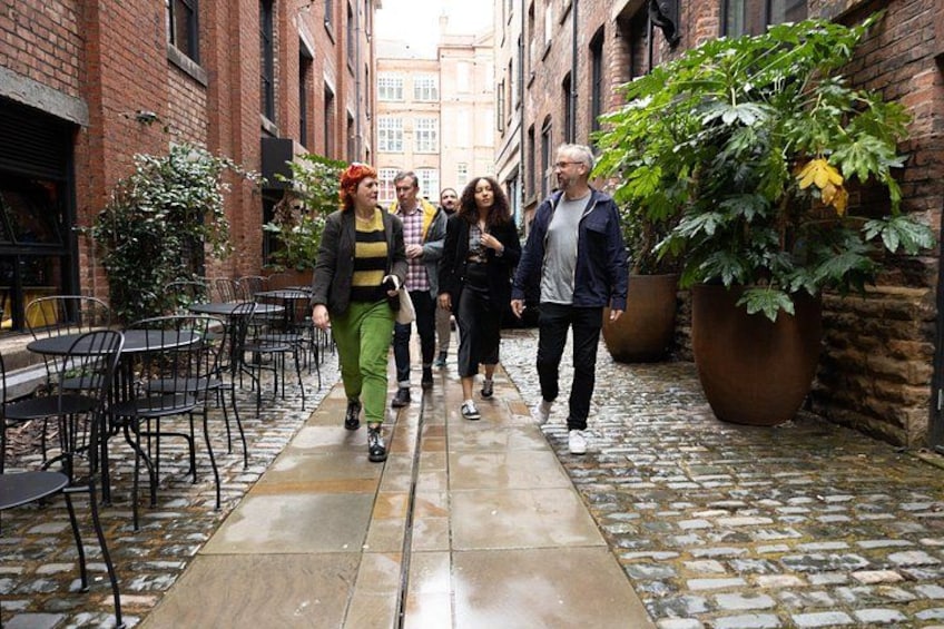 A narrow alley with cobblestone pavement, brick buildings, outdoor seating, and potted plants. 4