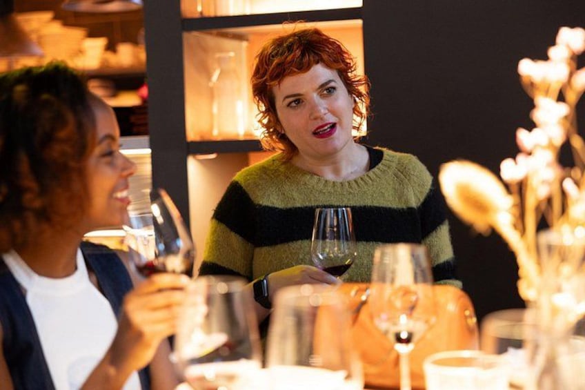 A person sitting at a table with a wine glass, surrounded by other people and a bookshelf in the background. 2