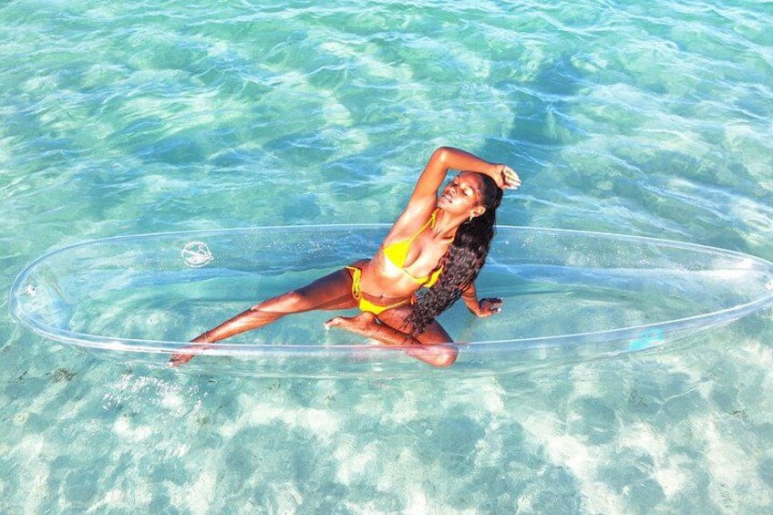A person in a yellow bikini lying on a transparent inflatable ring in clear blue water. 1