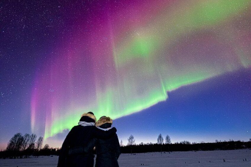 Two people observing the Northern Lights in a snowy landscape. 5