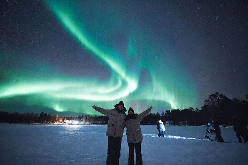 Two people standing on snow with the aurora borealis in the background. 3