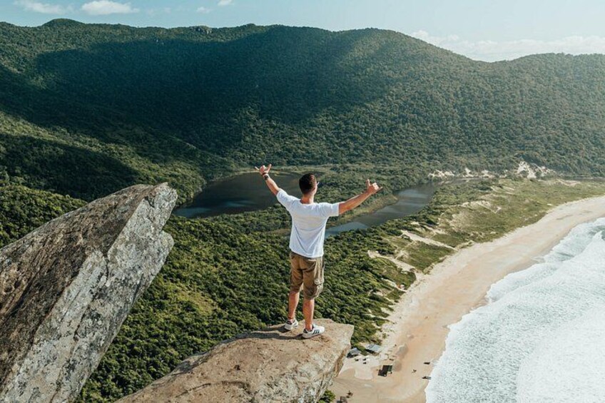 A person standing on a cliff overlooking a beach and a lake. 1