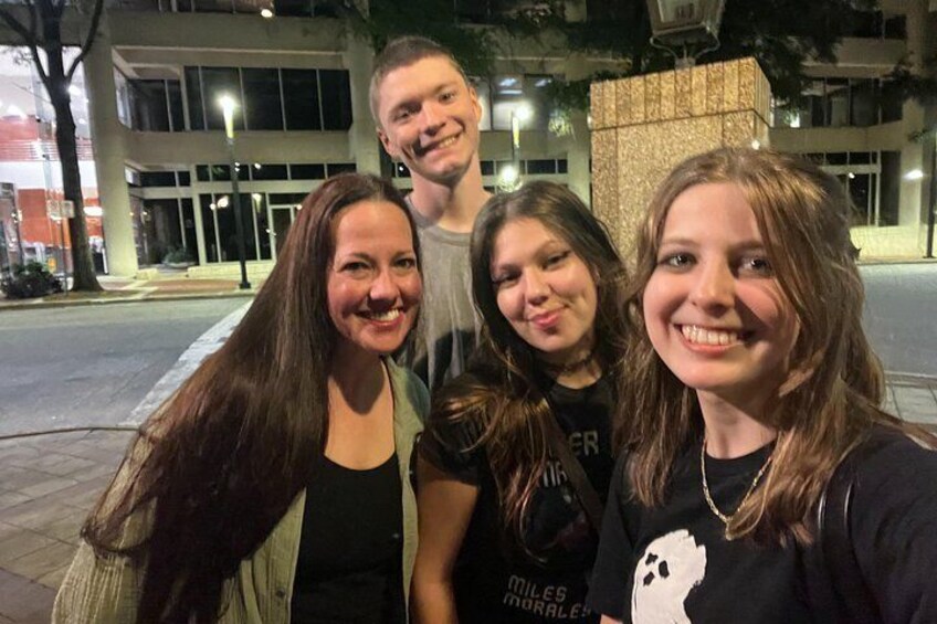 Four people posing for a photo on a city street at night. 2