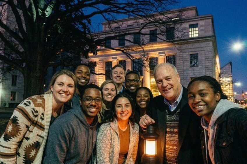 A group of people posing in front of a historic building at night. 1