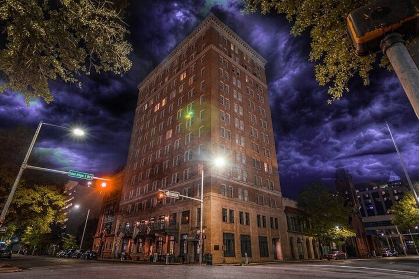 A tall brick building with illuminated windows at night, surrounded by trees and streetlights. 5