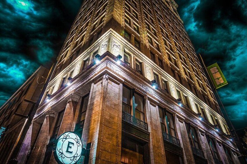 A tall building with illuminated windows and a large circular sign with the letter 'E' at the base. 3