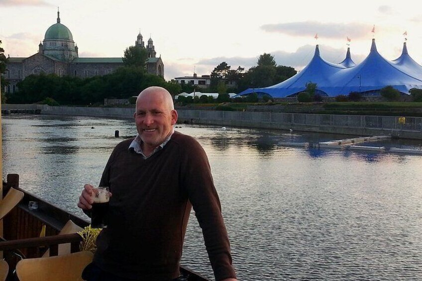 A man on a boat, a river, and a building with a dome and blue tents in the background. 5