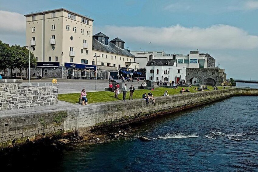 A waterfront promenade with people walking, a stone wall, and buildings in the background. 4