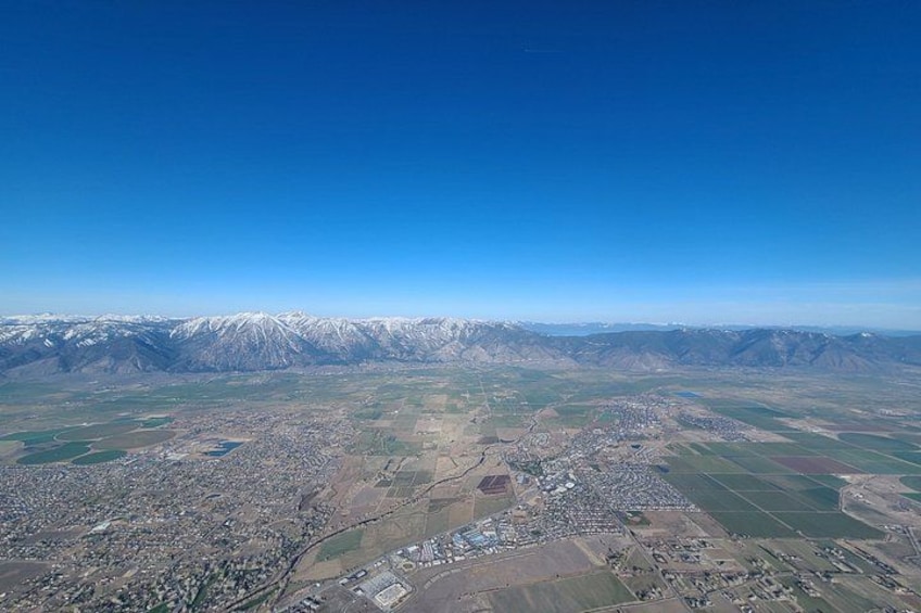 Un paisaje montañoso con picos nevados, un pueblo con edificios y campos de cultivo. 2