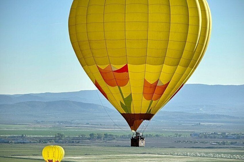 Un globo aerostático con diseño amarillo y rojo, volando sobre un paisaje llano con montañas a la distancia. 3