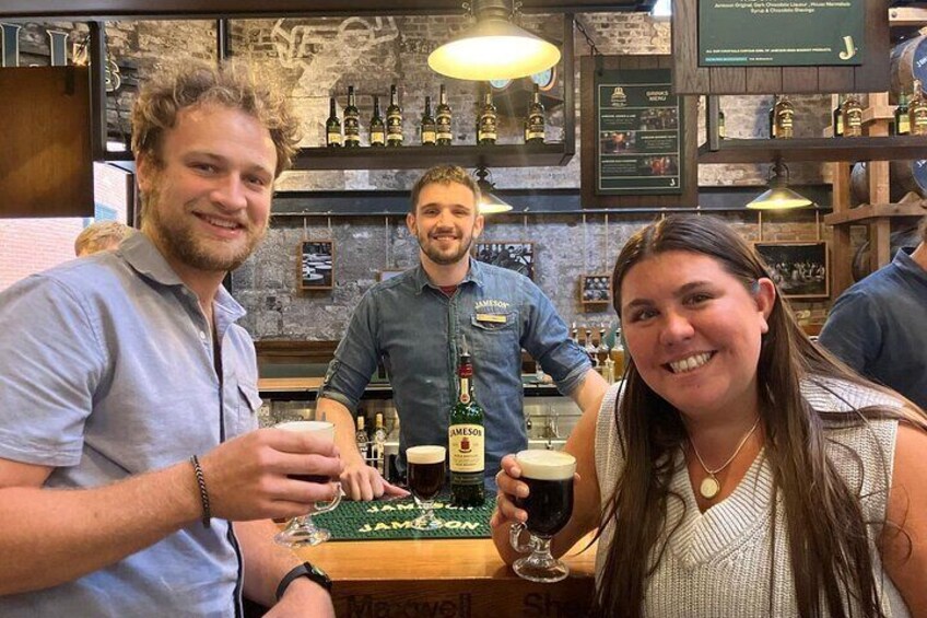 A bar with people holding drinks, a bartender, and shelves with bottles. 2