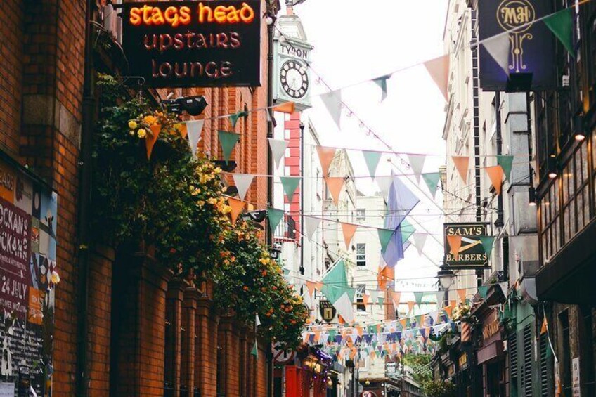 A narrow street with buildings, a clock, and bunting flags. 5