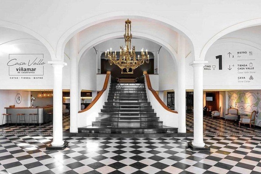 A grand staircase with a chandelier, white columns, and a checkered floor. 2