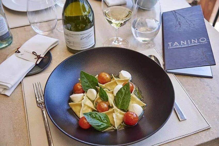 A plate of pasta with cherry tomatoes and basil, a wine bottle, and glasses on a table. 3