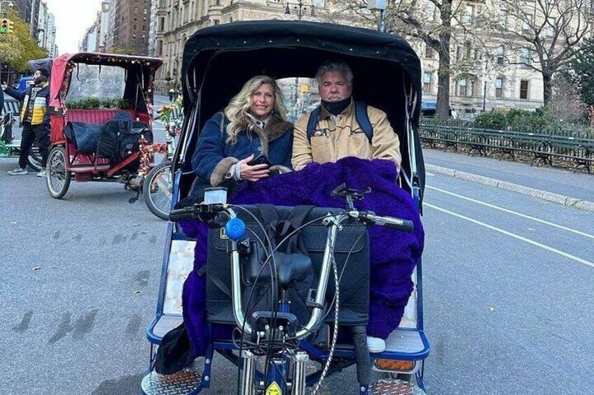 Une personne vêtue d’un manteau violet, assise dans une calèche noire, avec un vélo à proximité. 2