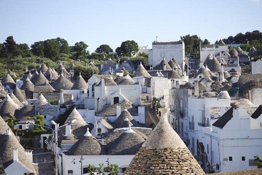 A village with numerous conical-roofed buildings, a clear sky, and a hilly landscape in the background. 1