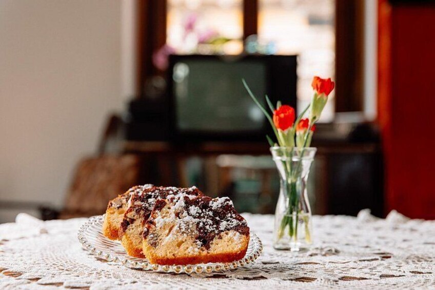 A pastry on a glass plate, a lace tablecloth, and a vase with red flowers. 5