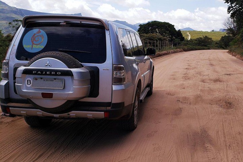 A silver Pajero SUV parked on a dirt road with a scenic landscape in the background. 2